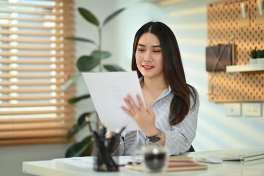 Charming asian female accountant working bookkeeping documents, checking financial data at office.