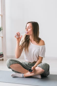 Young beautiful girl practicing yoga at mat, drinking water while break. Fitness and healthy lifestyle concept