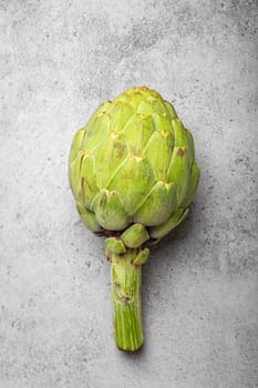 Fresh raw organic farm one artichoke on grey rustic stone background top view, healthy artichokes in balanced nutrition and cooking concept