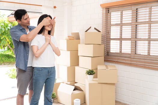 Smiling young Asian happy couple close girlfriend eyes for a surprise at moving day in their new home after buying real estate. Concept of starting a new life for a newly married couple.