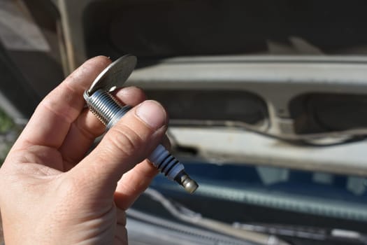 Hand Gapping a Spark Plug in Front of Car . High quality photo