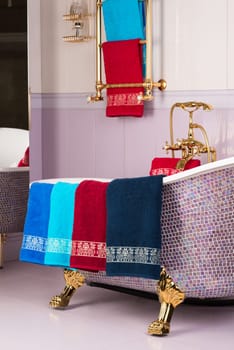 A vertical shot of colorful bamboo towels hanging on a mosaic purple bathtub in a bathroom