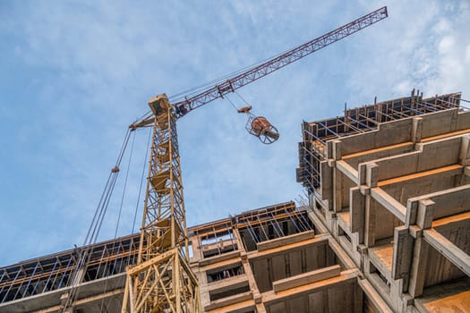 A low angle shot of a crane with equipment on a construction site with a new building infrastructure. Pouring concrete into a mold