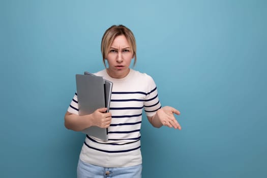 horizontal photo of an indignant business woman in a casual striped sweater with a portable computer laptop in her hands on a blue background.