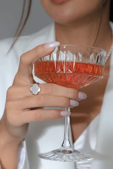 A vertical shot of a Caucasian female holding a cocktail glass with a ring on the finger
