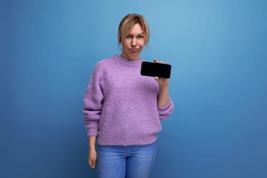 distressed blond young female consultant in purple hoodie holding smartphone with mockup on blue background with copy space.