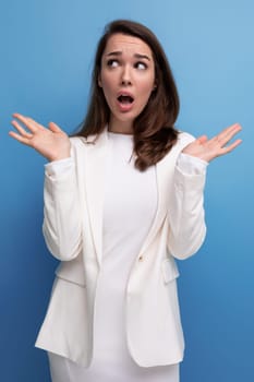 surprised confused pretty brunette young woman in a dress and jacket with a grimace.