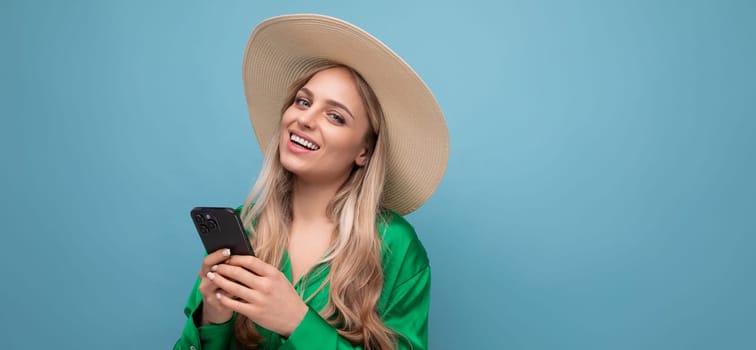 cute young woman on vacation in a summer straw hat with a phone on a blue studio background with.