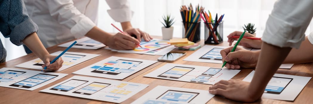 Panorama shot of front-end developer team brainstorming UI and UX designs for mobile app on paper wireframe interface. User interface development team planning for user-friendly UI design. Scrutinize