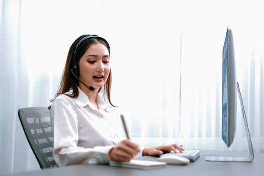 Asian call center with headset and microphone working on her laptop. Female operator provide exceptional customer service. Supportive call center agent helping customer on inquiry. Enthusiastic