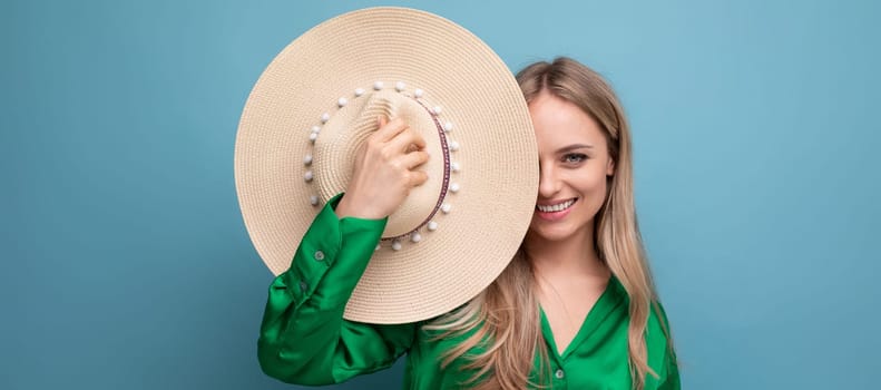 smiling woman on vacation holding a straw hat near her face on a blue studio background.