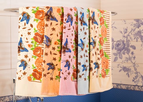 A row of colorful patterned towels hanging on a shower rack above a bathtub