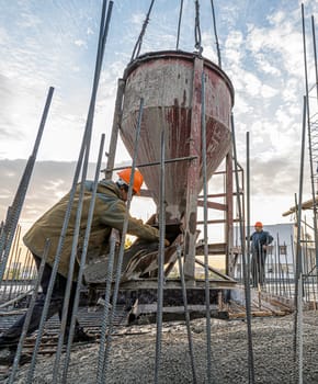 The workers on a building infrastructure roof with machinery and tools. Pouring concrete into a mold