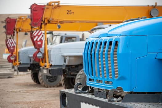 A closeup row of large truck cranes and machines at an industrial construction site