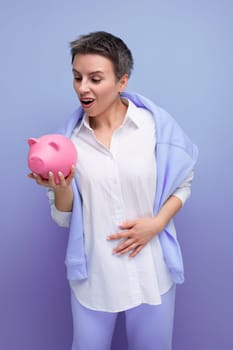 nice young lady with short hair plays with pink piggy bank.