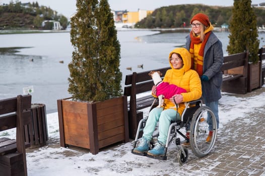 A woman in a wheelchair walks with her friend and a dog by the lake in winter