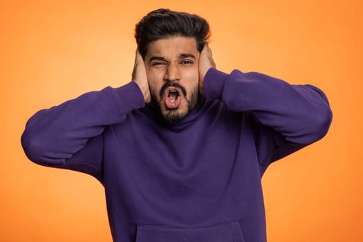 Dont want to hear and listen. Frustrated annoyed irritated indian man covering ears gesturing No, avoiding advice ignoring unpleasant noise loud voices. Handsome hindu guy alone on orange background
