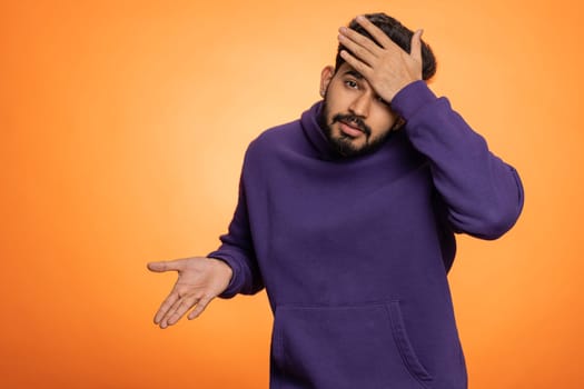 Face palm. Shame on you. Upset surprised young indian man making face palm gesture, loses, feeling bored, disappointed in result, bad news. Handsome hindu guy isolated on orange background, indoors