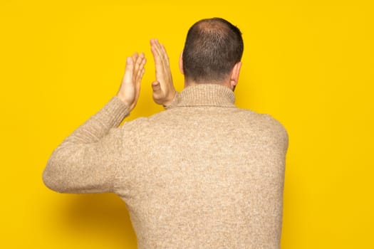 Man with alopecia problem energetically patting his back, excited by the spectacle he has just witnessed. Isolated on yellow background.