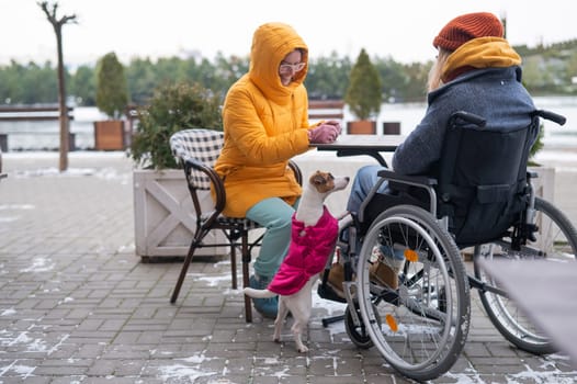 Two girlfriends in a cafe on a street terrace in winter. Woman in a wheelchair