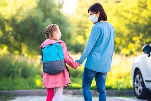 Mother meeting primary schoolgirl after classes on car parking outdoors during virus epidemic
