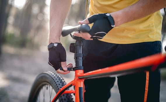 Rider adjusting seat height on bicycle standing in sunny forest
