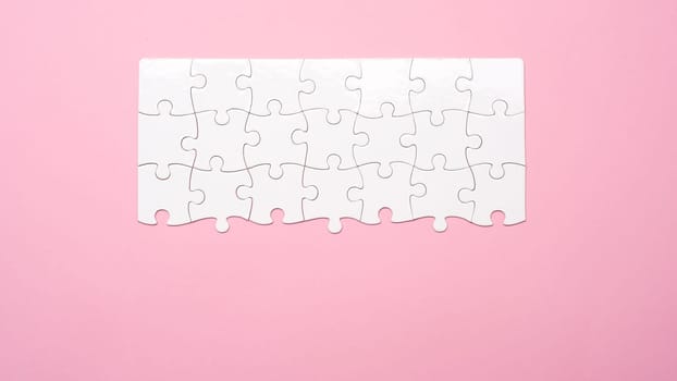 Top view of unfinished white jigsaw puzzle on pink background with copy space