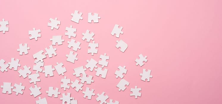Scattering of white jigsaw puzzle pieces on pink background with copy space, top view