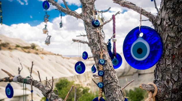 Amulets against evil eye hanging on tree in front of sandy mountain in Cappadocia, Turkey