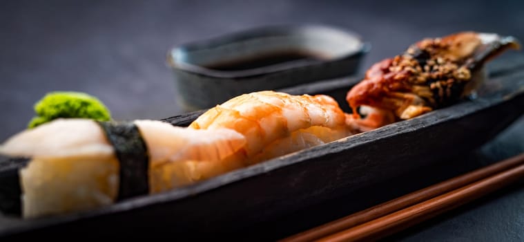 Sushi sashimi set with shrimps and soy sauce served with wooden chopsticks and wasabi on black table. Traditional japanese meal with rice and seafood closeup