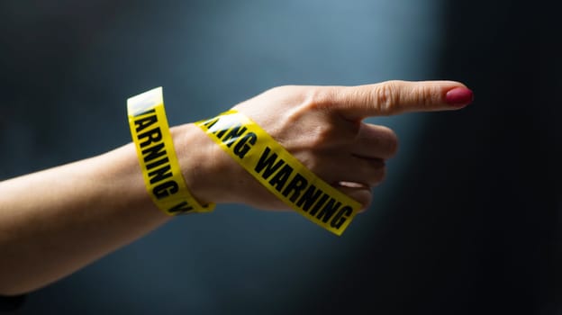 Hand wrapped with yellow caution tape with warning words shows direction with finger