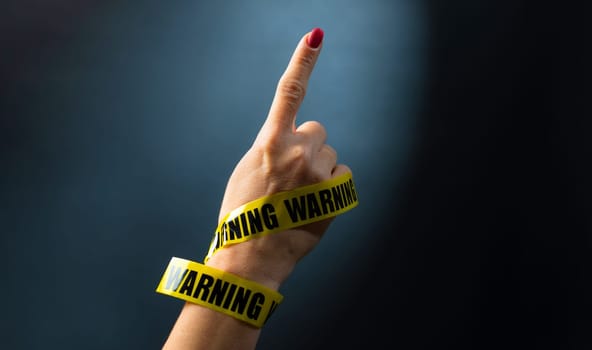 Hand wrapped with yellow tape with warning words shows with finger up. Concept of caution and protection