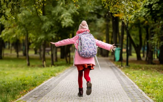 School girl with backpack running at autumn park. Preteen child having fun oudoors