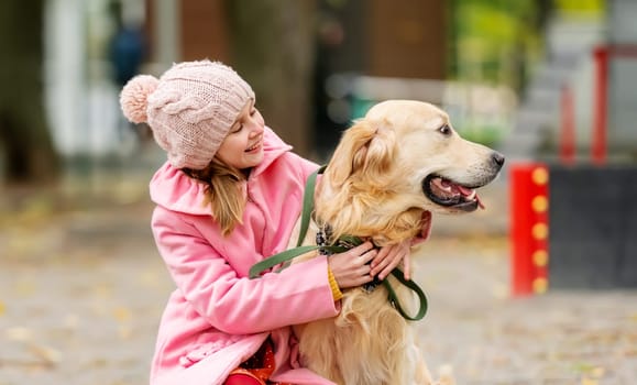 Preteen girl kid with golden retriever dog sitting in the park and hugging doggy. Female child with pet at autumn