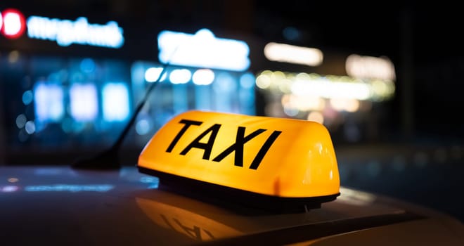 Taxi car light on dark street at night closeup. Cab sign on the vehicle roof glowing in the dusk outdoors