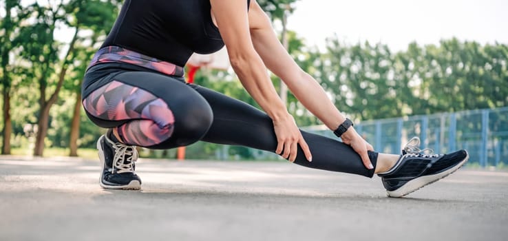 Young girl woman doing stretching outdoors preparing for active fitness workout. Female sportsman exercising at stadium outside in summer time