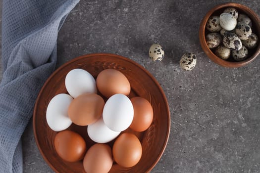 Chicken and quail eggs on a plate on a concrete background with textiles.