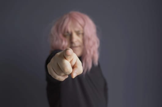 Portrait of a man in a pink wig, looking and pointing his finger at the camera. close-up.