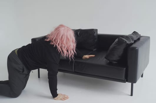 A drunk man in a pink wig crawls across the floor to the sofa, sleeps on the sofa.