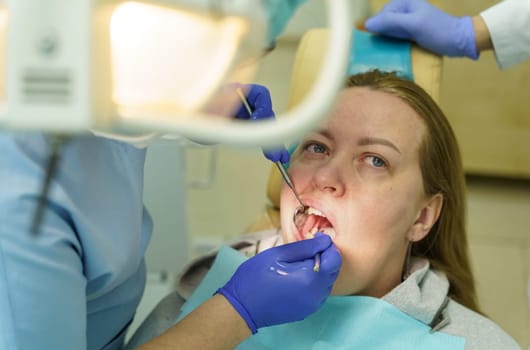 A doctor examines a woman's teeth with a dental instrument. Close-up