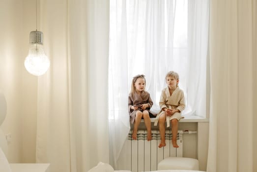 A boy and a girl in bathrobes are sitting on the windowsill, talking, playing.