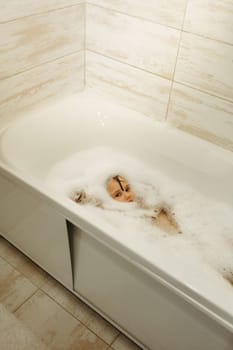 Happy little girl swims in a bathtub full of foam. Only the face is visible from the foam.