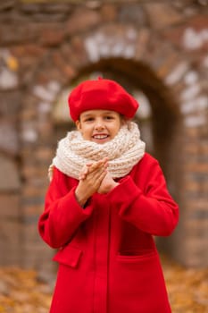 Caucasian girl in a red coat and beret is freezing on a walk in the autumn park