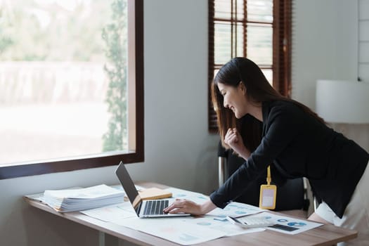 Portrait of a woman business owner showing a happy smiling face as he has successfully invested her business using computers and financial budget documents at work.