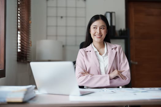 Portrait of a woman business owner showing a happy smiling face as he has successfully invested her business using computers and financial budget documents at work.