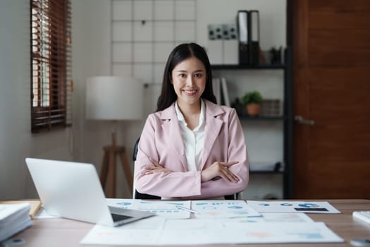 Portrait of a woman business owner showing a happy smiling face as he has successfully invested her business using computers and financial budget documents at work.