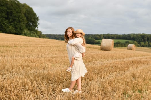 Mother holds daughter in her arms in a field with wheat Mothers day