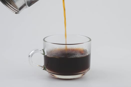 Pouring coffee from moka pot into transparent glass isolated on white background. Close-up of hand pouring freshly brewed drip coffee in a mug. Prepare alternative coffee.