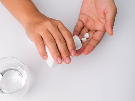 Close-up of woman pouring pills from bottle for medicinal purposes. Woman holding pills in hand with water. Healthcare, medicine, treatment, therapy concept