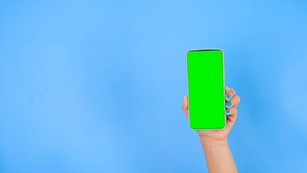 Female hand holding smartphone with mockup green screen on blue background. Close-up woman hand use smartphone with mock-up for Swiping or Watching content. Chroma key mock-up on smartphone in hand.